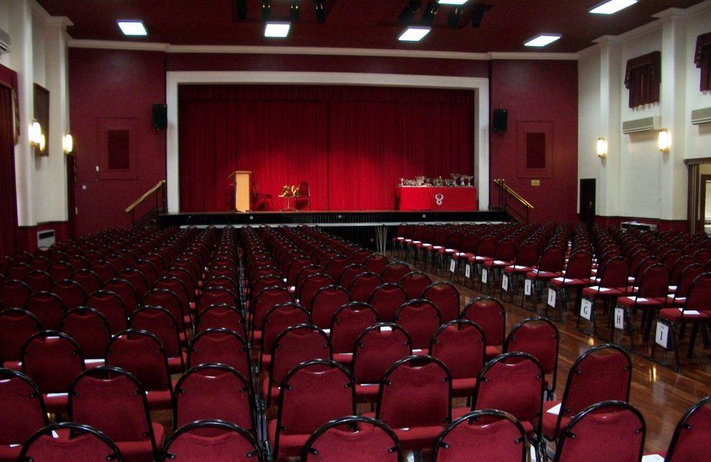 Chairs laid out in Sir James Hawkey Hall in an audience format facing the stage , all the chairs and the stage are empty