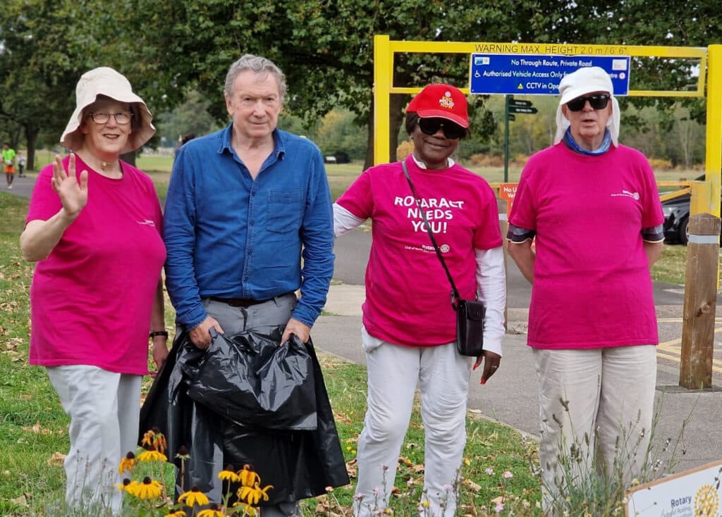 community action day, 4 people standing and smiling at the camera, one holding a bin bag, all stood infant of flower bed in a park